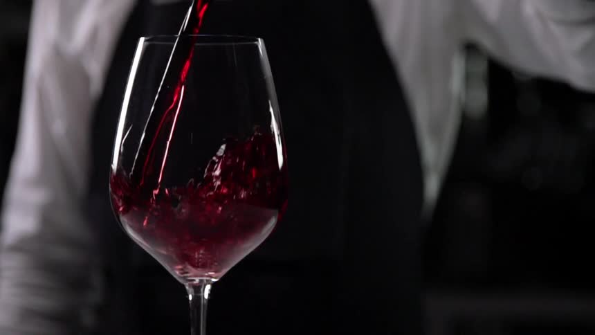 A bartender fills a glass with red wine