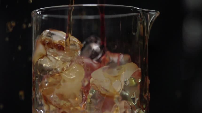 Drink being poured in a clear glass pitcher filled with ice