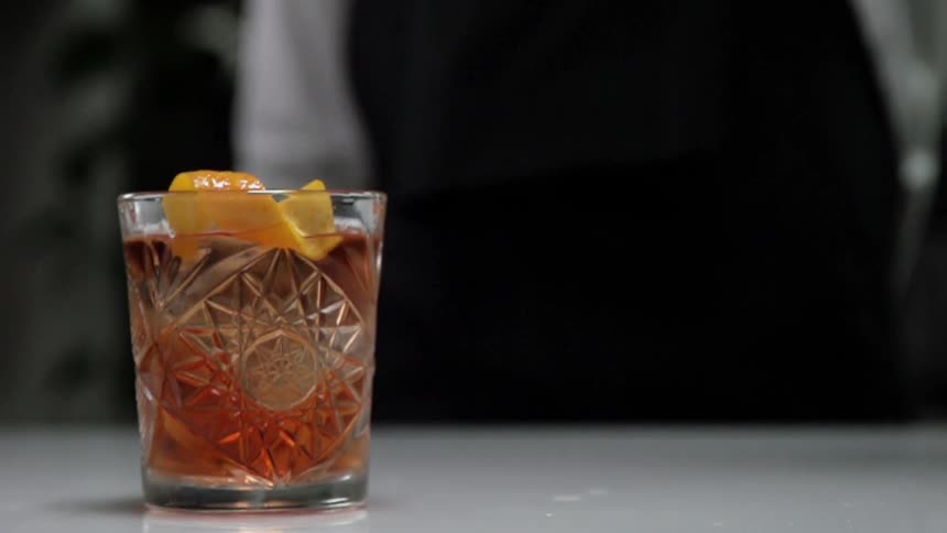 A bartender drops a twist of orange peel into a drink