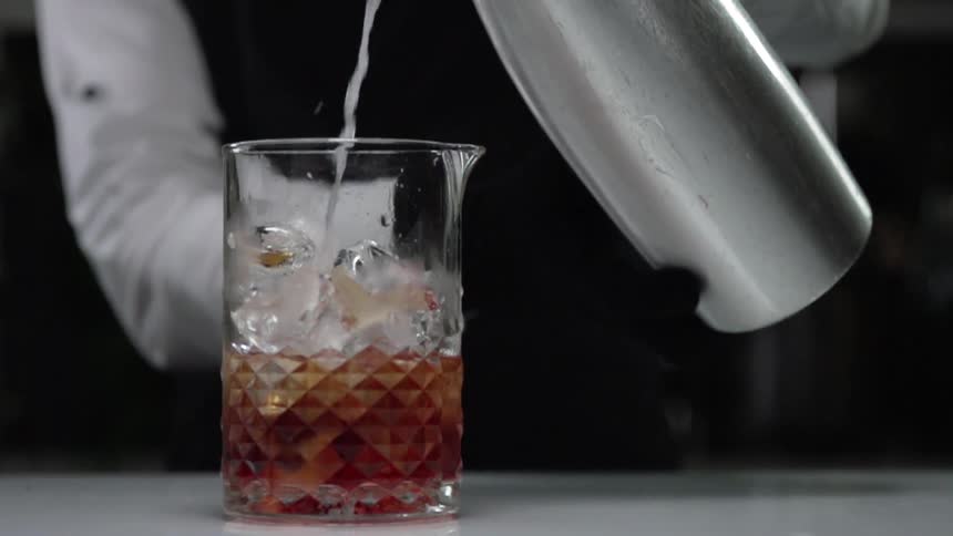 A bartender pours a drink into a glass filled with ice cubes