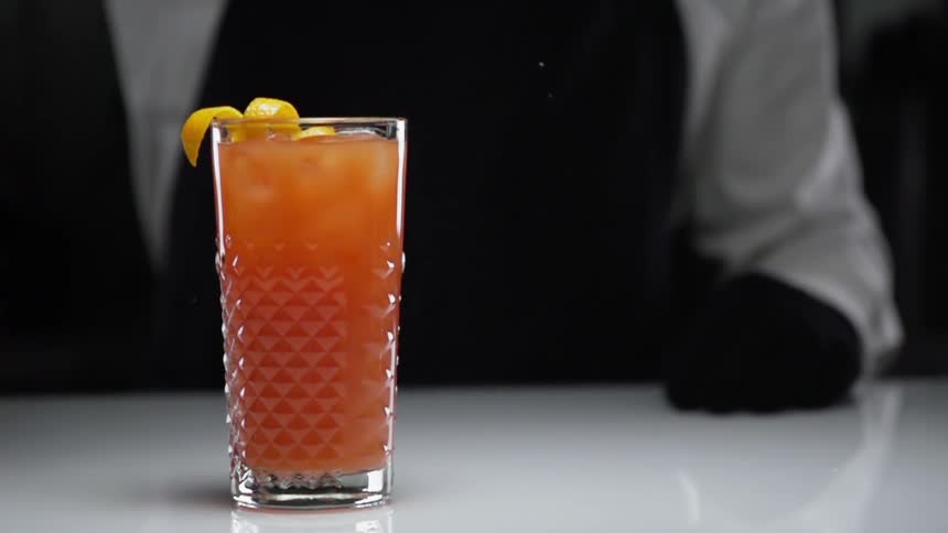 A person behind a drink as lemon peel falls in to it