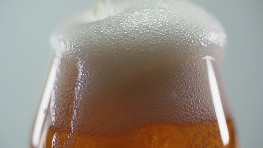 A large head of foam builds on a glass of beer as more pours into the glass