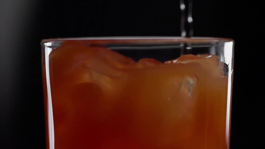 A metal stirrer moves through a glass filled with liquid and ice cubes