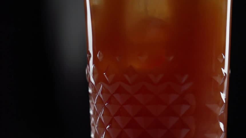 Orange and red liquid and ice cubes swirl in a beveled glass