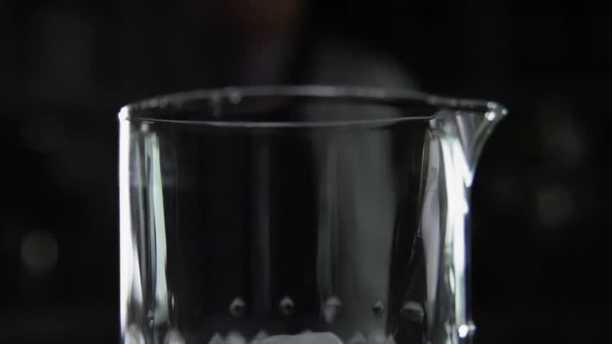 An ice cube hits the sides of a clear mixing glass as it falls in
