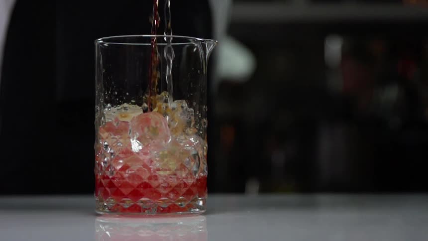A person pours a cocktail in to a glass