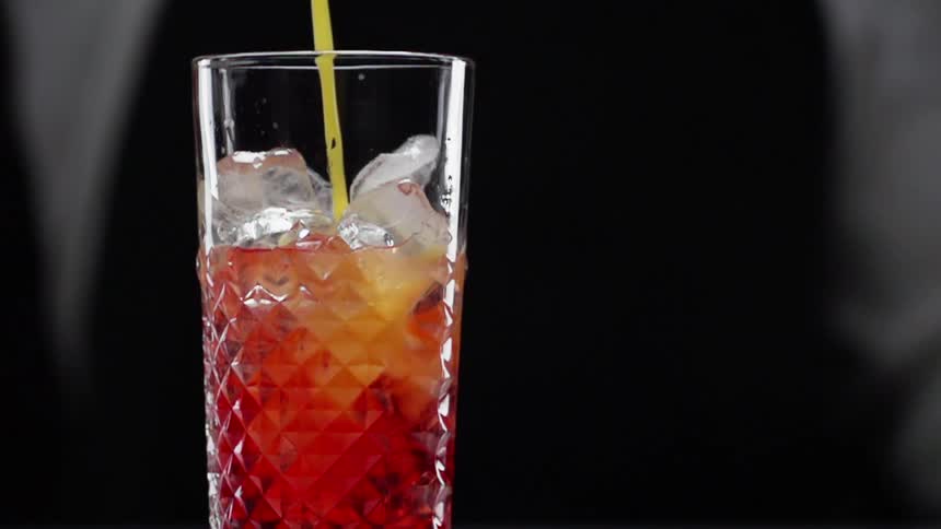 A cocktail is being poured into a glass full of ice cubes