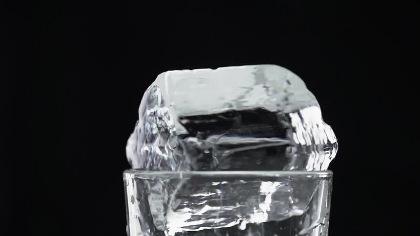 An ice cube circling on the rim of a glass with a black background