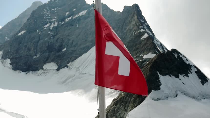 A red flag is blowing in the wind on top of a snowy mountain