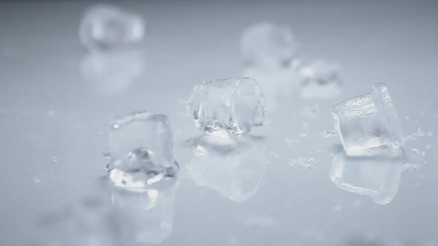 Ice cubes fall down and slide away on a white surface