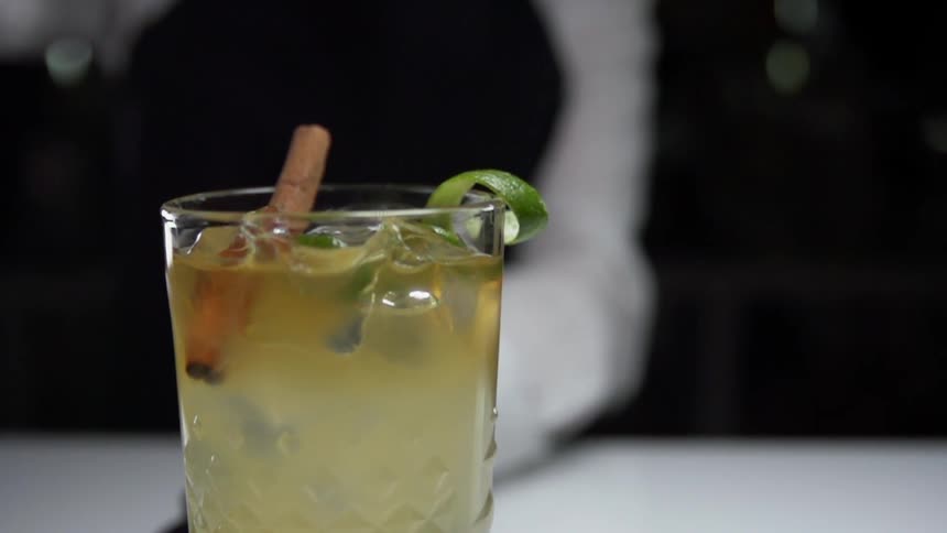 A person stands behind a beverage on a counter as mint is dropped in to it