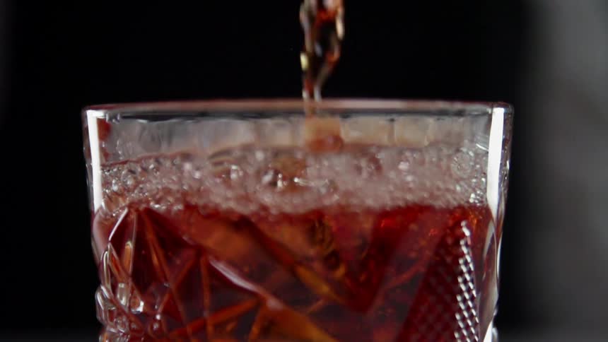 The glass is being filled with reddish liquid