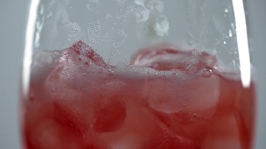 A drink being poured in to a glass with ice