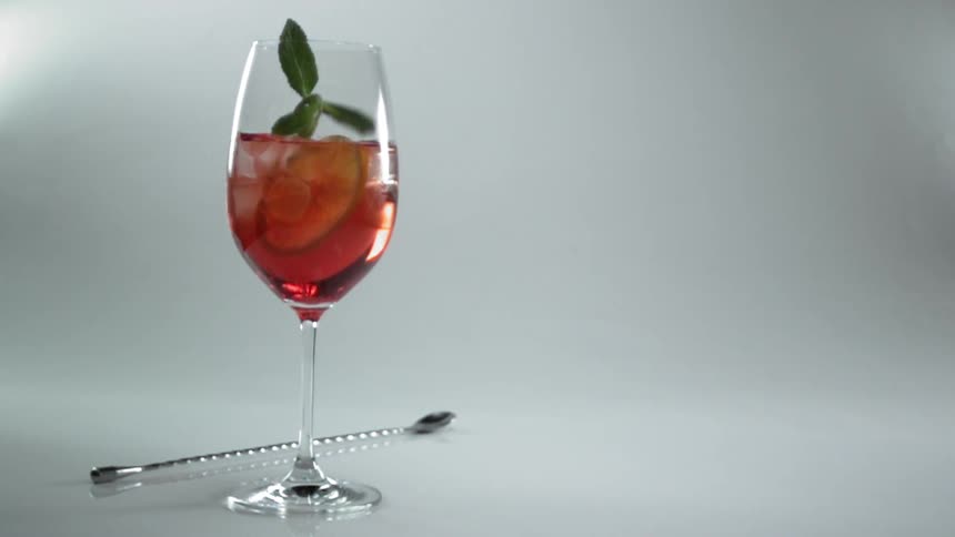 A leaf falls into a wine glass with a red liquid a lime peel and ice