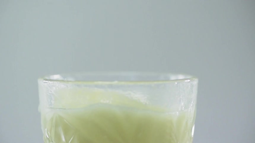 An ice cube drops into a glass filled with a green drink