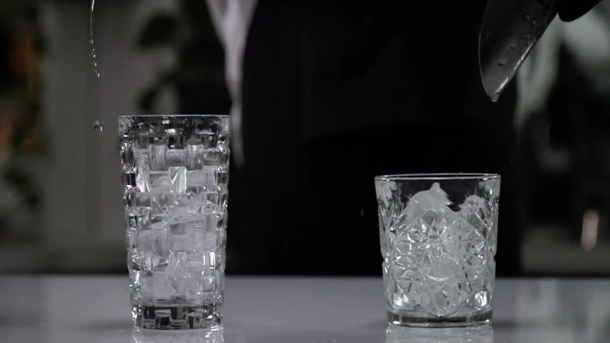 The bartender pours the ice into the glasses