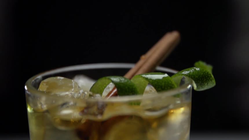 A twist of lime peel drops into a cocktail