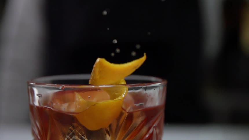 Thin citrus drops into amber iced beverage spraying droplets