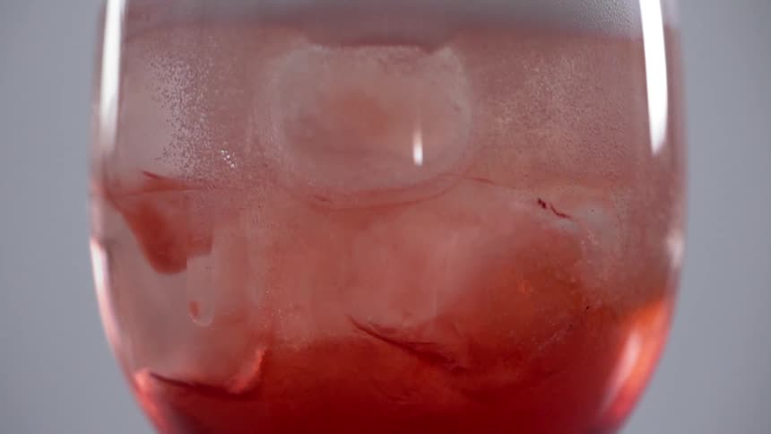 Ice cubes float in a glass filled with a rose colored drink
