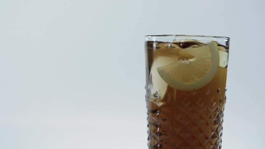 A lemon falling into a glass of amber liquid