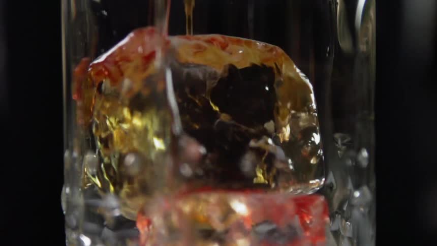 Cocktail is being poured into a glass full of ice