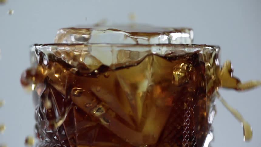 A very large ice cube dropped into a small glass of liquor