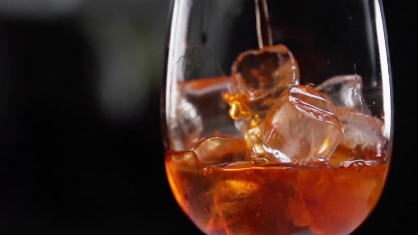 A bartender pours liquid into a wine glass filled with ice cubes