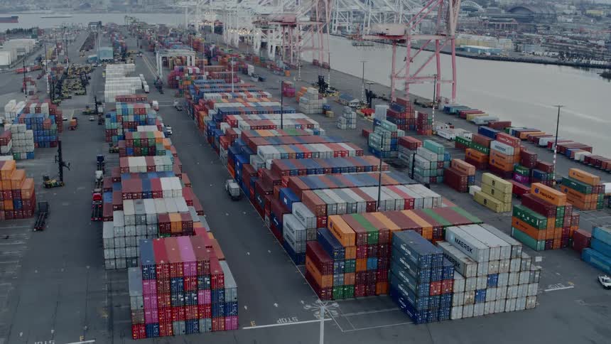 Tilt up pullback reveal from stacks of colorful cargo containers to reveal a busy international shipping terminal