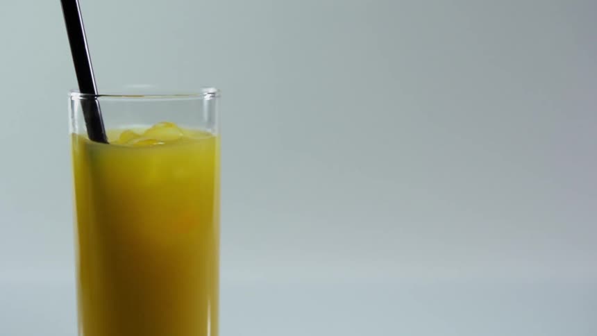 A straw being inserted into a narrow drinking glass filled with ice and yellow liquid