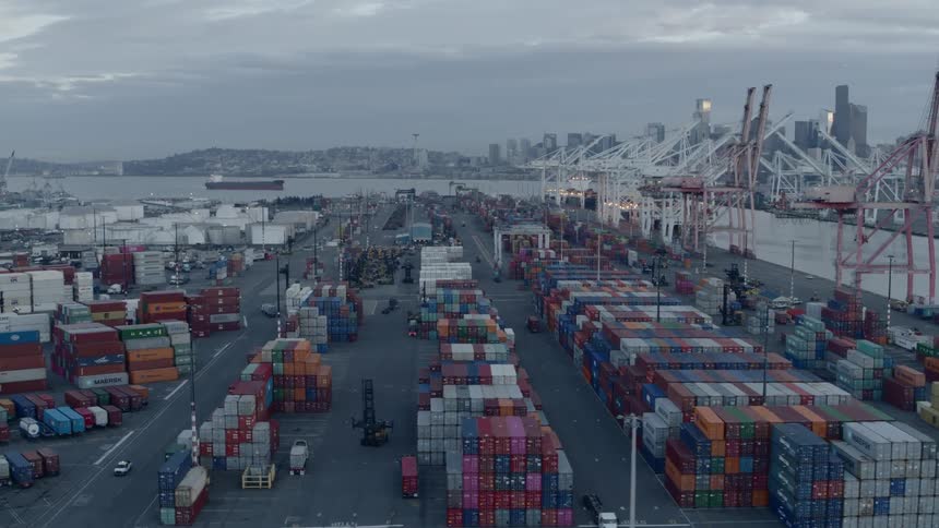 Trucks and forklifts drive through a large waterfront shipping facility