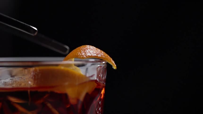 Barman puts the orange peel into the cocktail