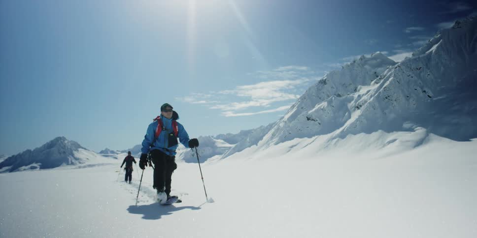 Two skiers move across a mountainous area covered in snow