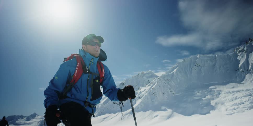 A man with skis walking in a valley covered with snow with another person behind