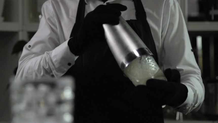 A bartender wearing an apron and gloves shakes a mixed drink