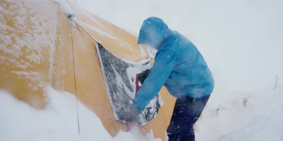 A person with a shovel removing snow from a yellow tent with a pirate flag