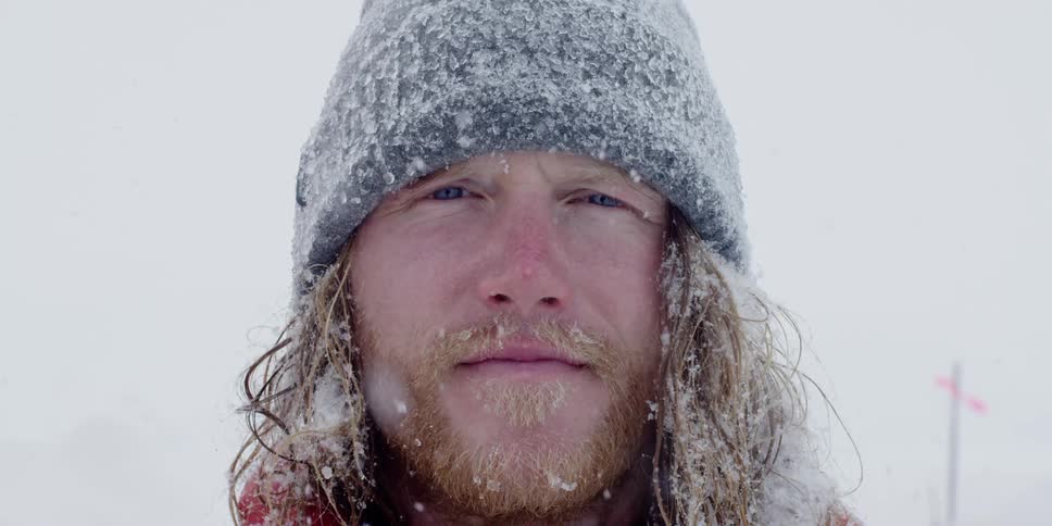 Man stands and looks at the camera while it snows