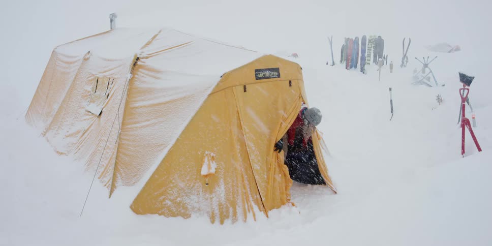 Person walking out of a tent in the snow during a snow storm