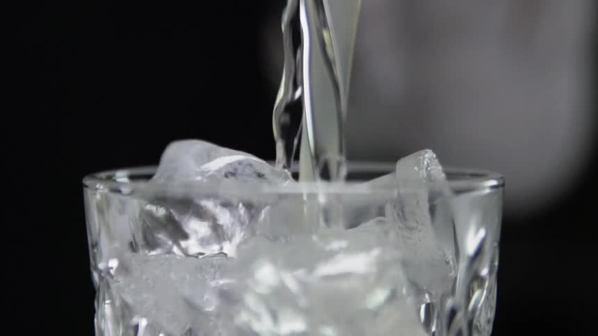 A bartender pours a mix of liquid and juice into a glass filled with ice cubes