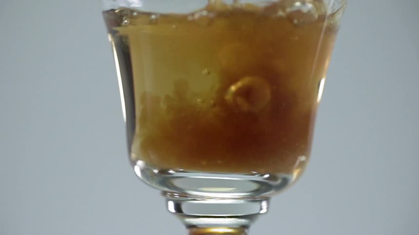 An amber liquid is poured into a cocktail glass mixing with a gold liquid