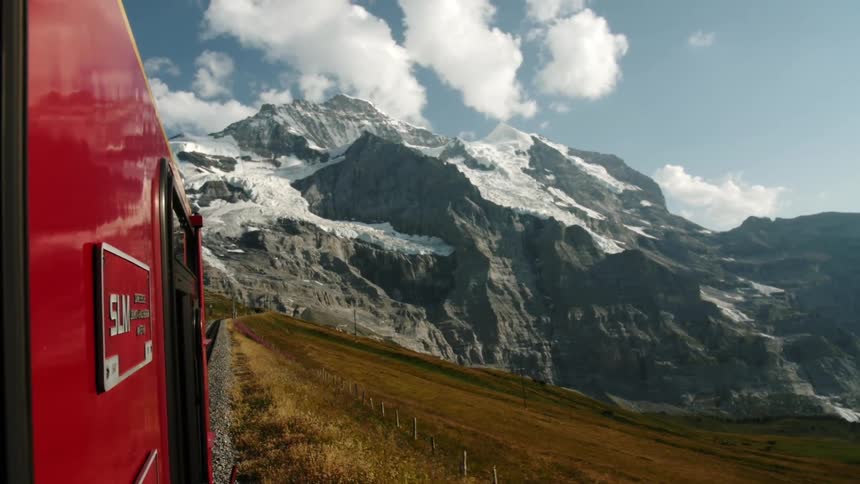 A train is traveling down some tracks with a mountain behind