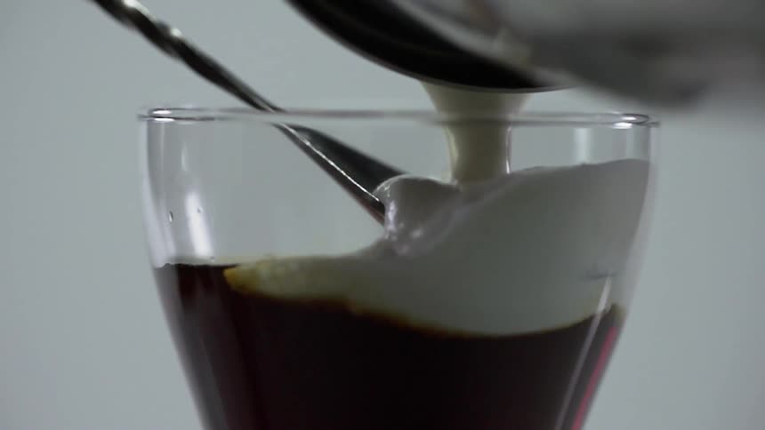 Cream is being poured on to a spoon and in to a beverage
