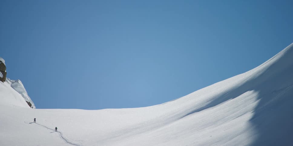 Two people walk up a snowy mountain