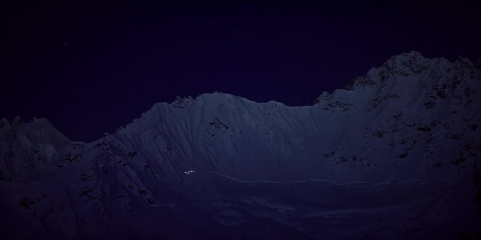 Timelapse of climbers zigzagging up a snowy mountain in the dark