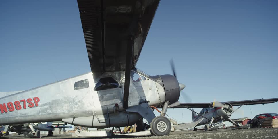 Two planes sit at an airfield with their engines running