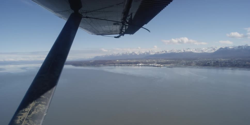 An aircraft flies over the water with mountains beyond