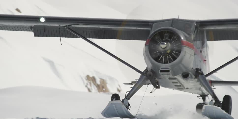 A small ski plane lands on deep snow in a mountain area