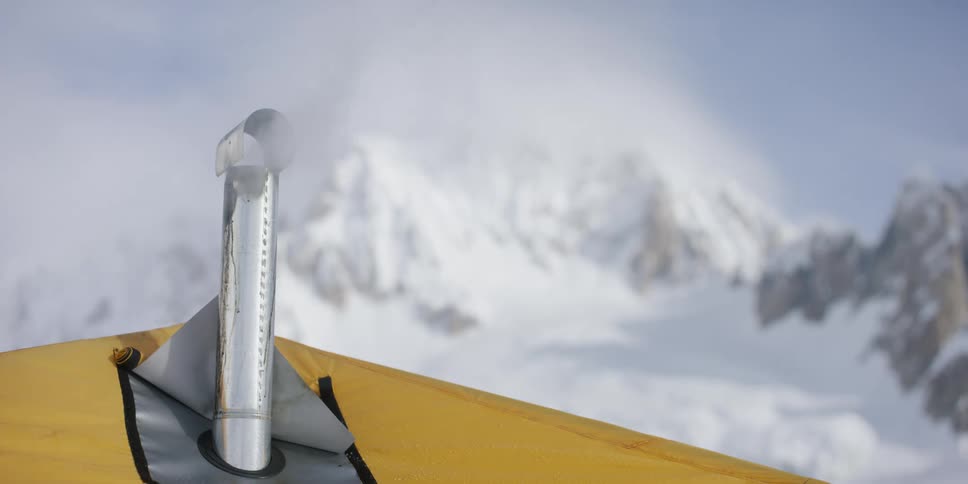 A tent stove pipe smokes in front of the mountains