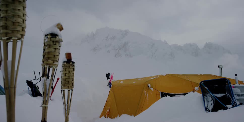 A campsite getting buried in the snow at the base of a mountain