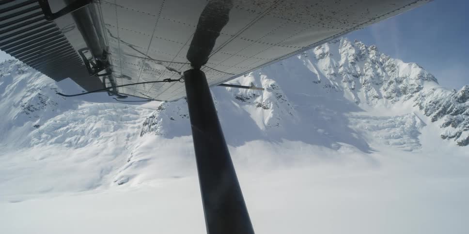 Aerial view of the snow capped mountain from under a wing of a flying light aircraft