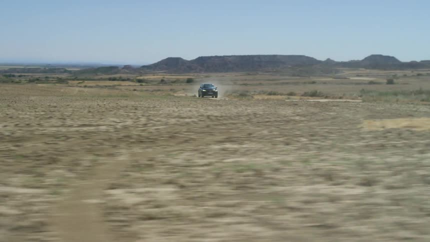 A vehicle driving in the desert with mountains in the background